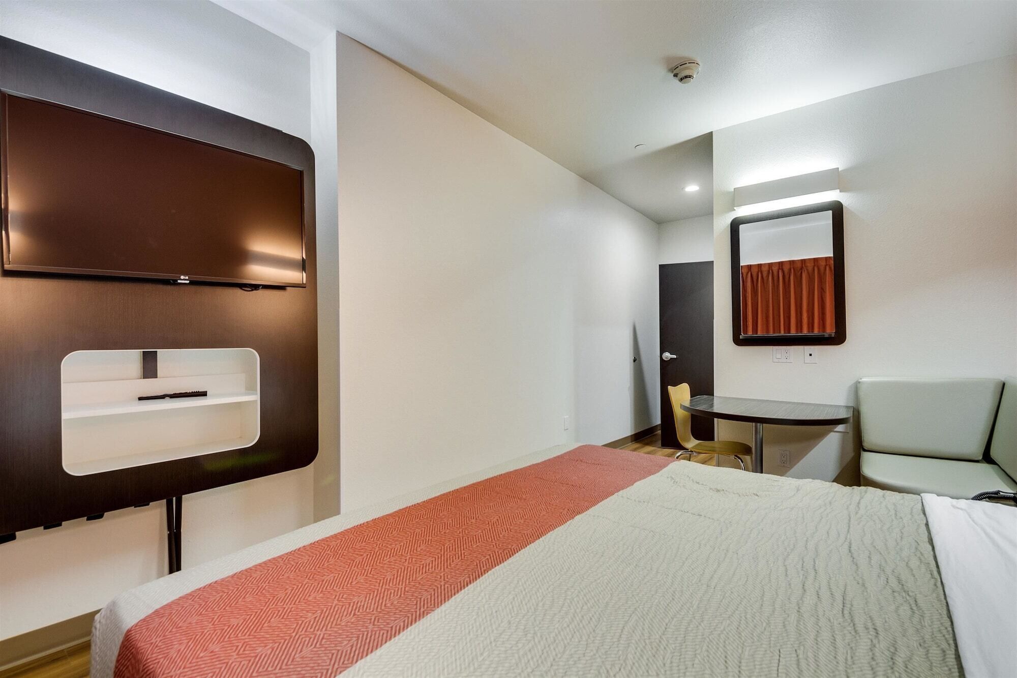 Een hotelkamer met een bed, een bureau, een stoel, een spiegel en een aan de muur bevestigde televisie.