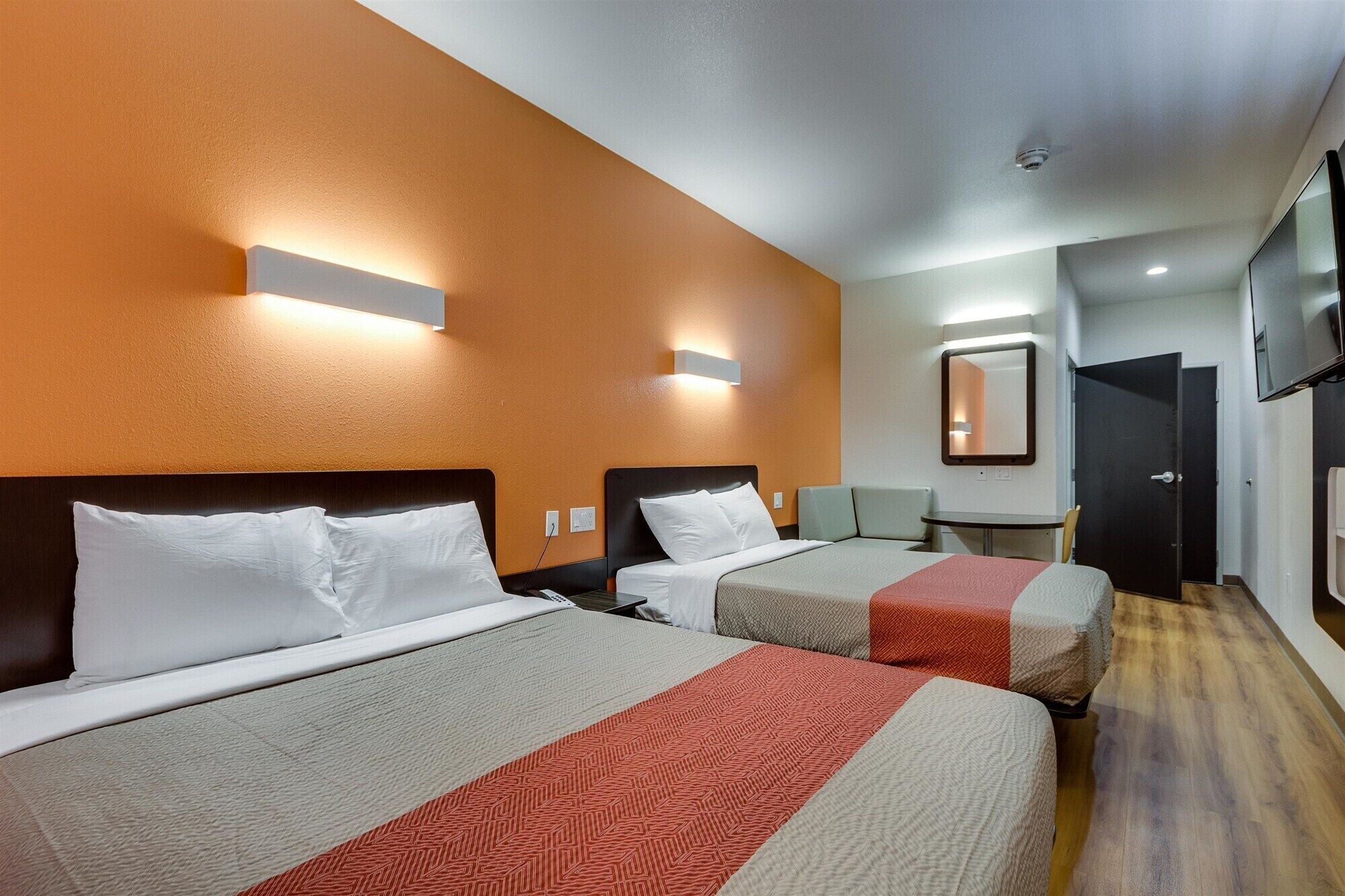 Une chambre d’hôtel avec deux lits, un bureau, une chaise, une télévision et un miroir.