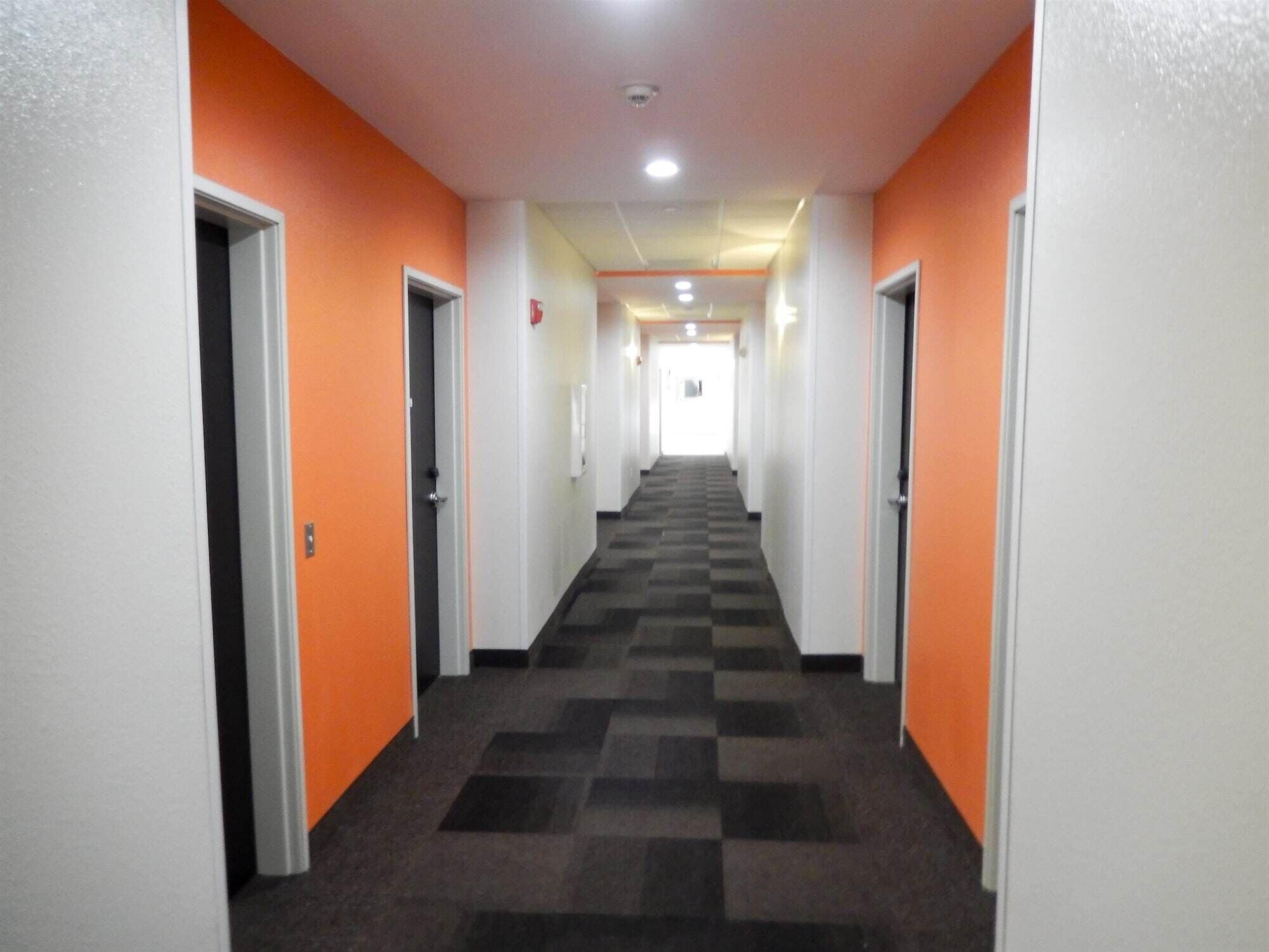 A hotel hallway with orange walls and a checkered carpet.