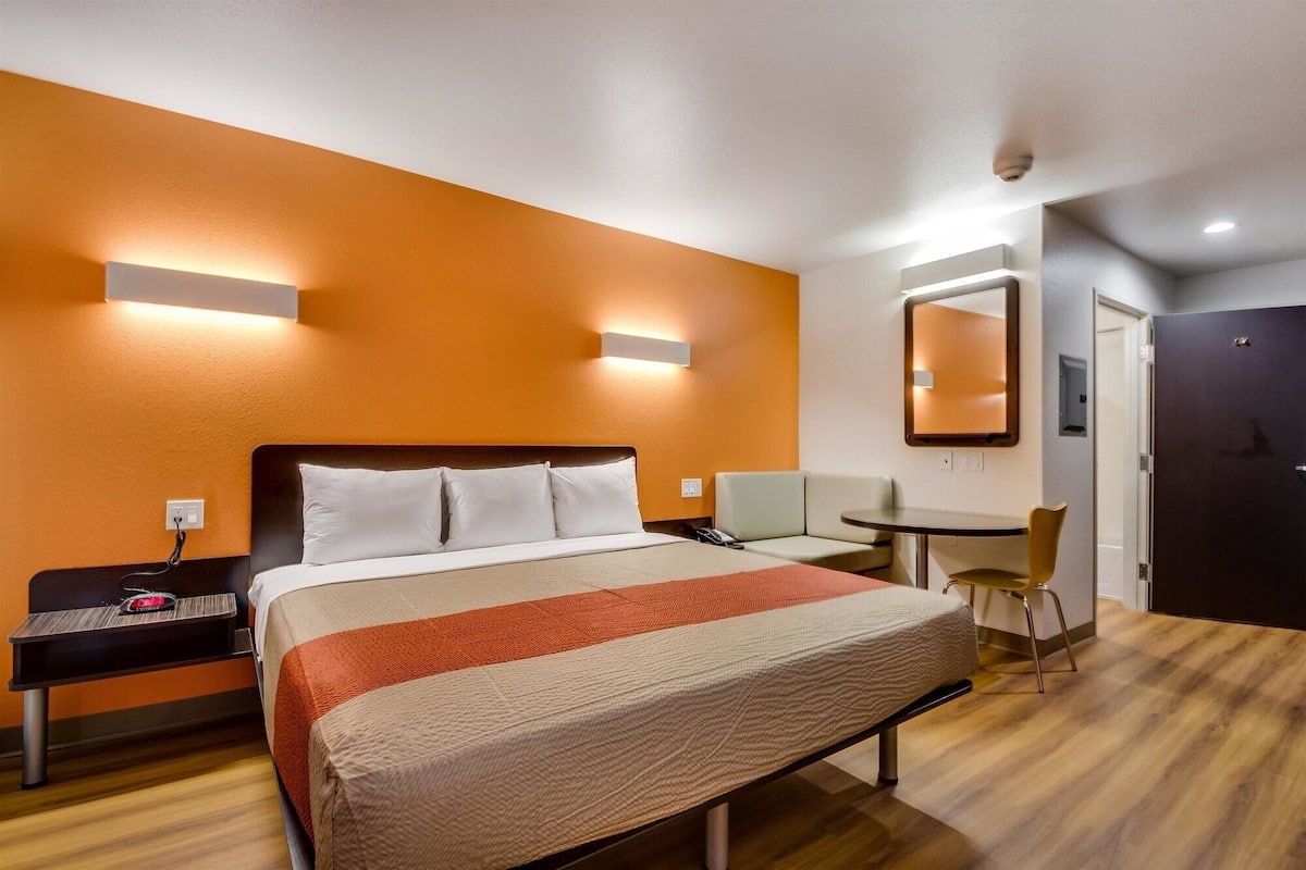 A hotel room with a bed, bedside table, chair, and a small desk with a chair.