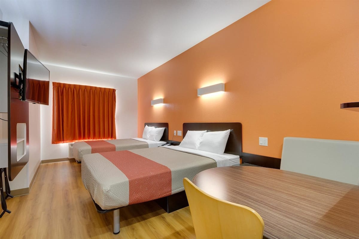 A hotel room with two beds, a TV, a table, and a chair.