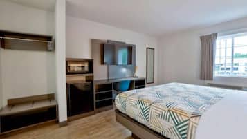 A modern hotel room with a bed, a TV, a desk with a computer, and a window with curtains.