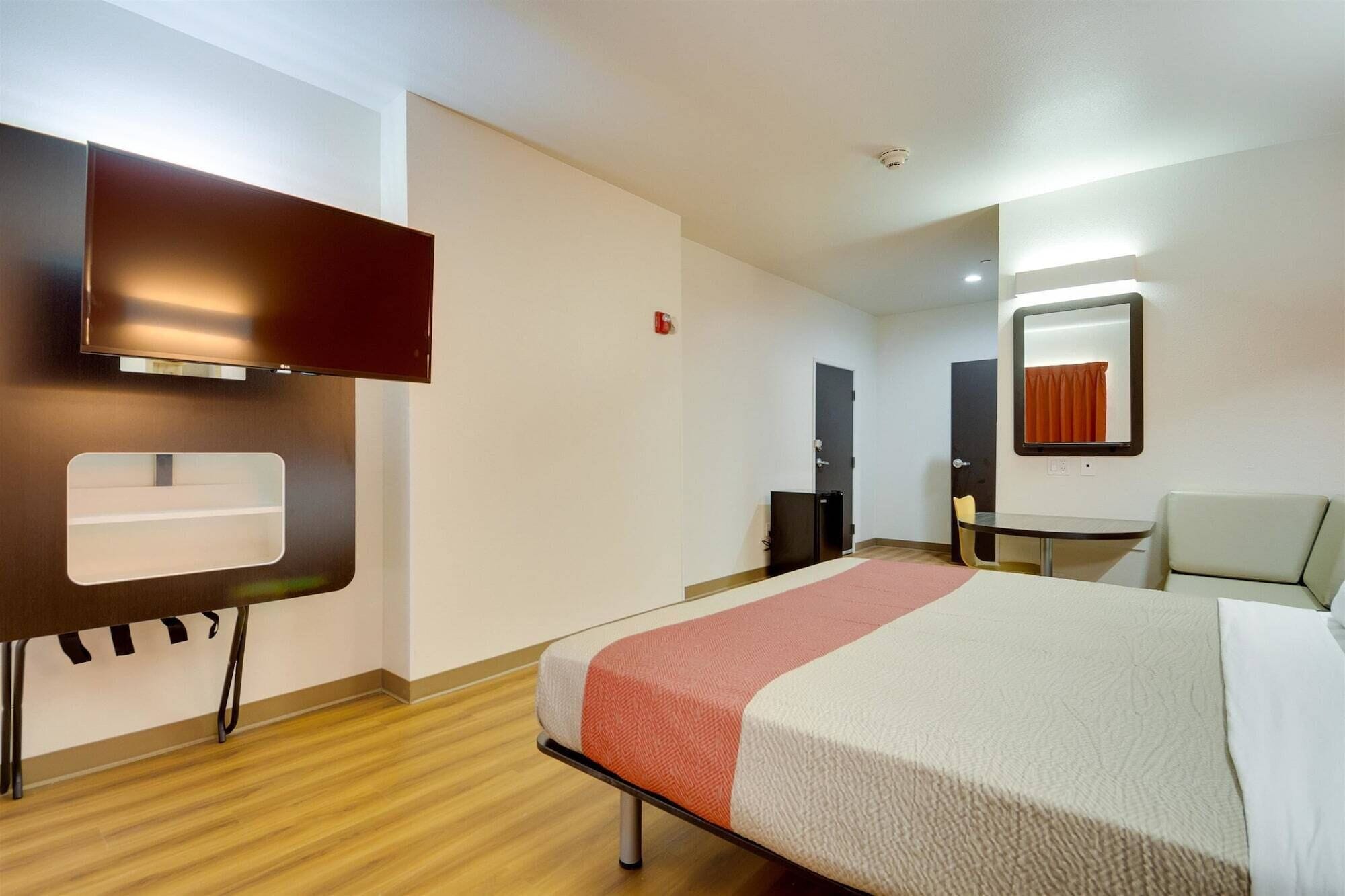 A hotel room with a bed, a desk, a chair, a television, and a mirror.