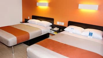 Two single beds with white linens, a bedside table with a phone and a lamp, and a wall-mounted light fixture.