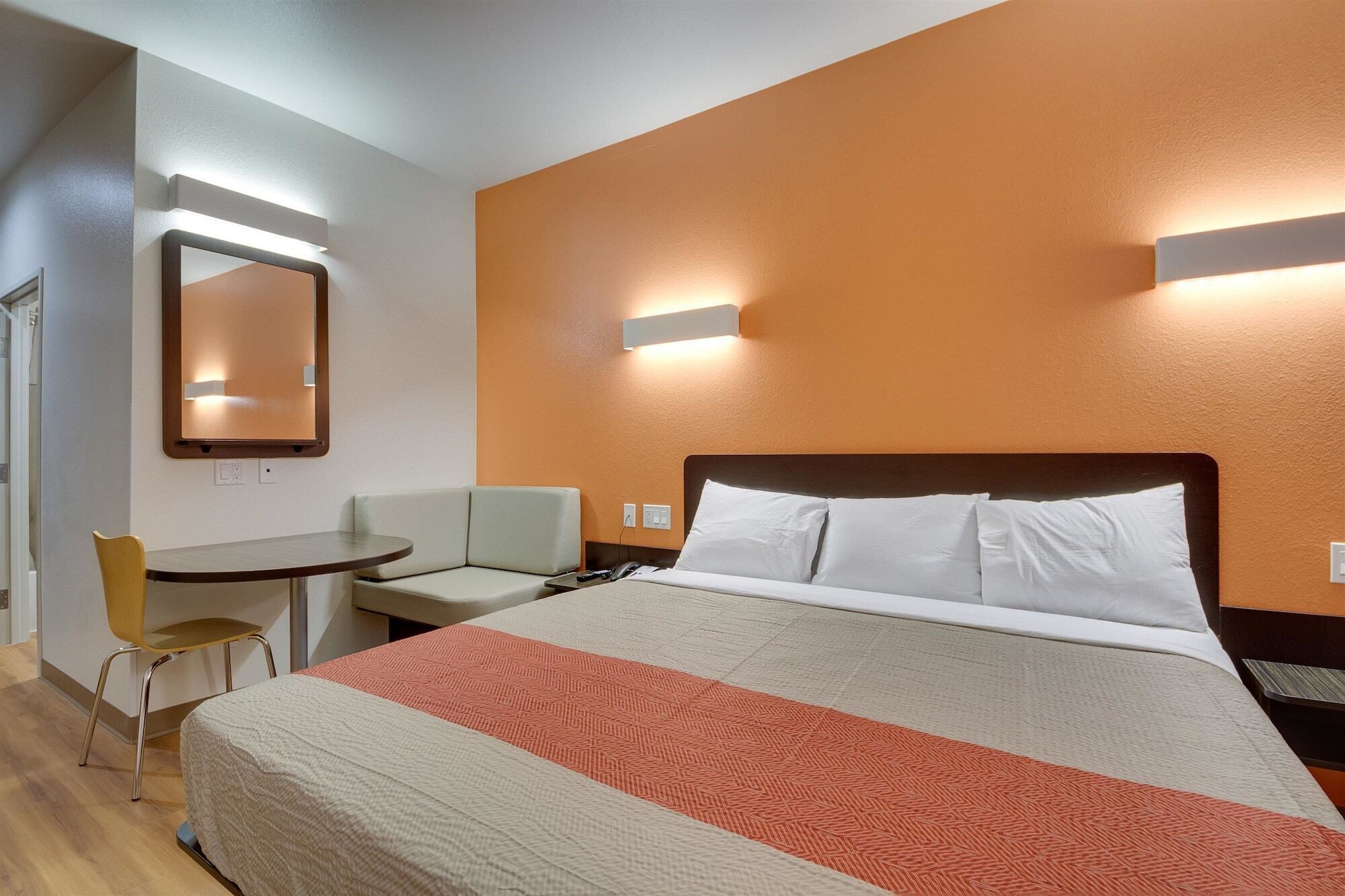 A hotel room with a bed, a desk, a chair, and a mirror.