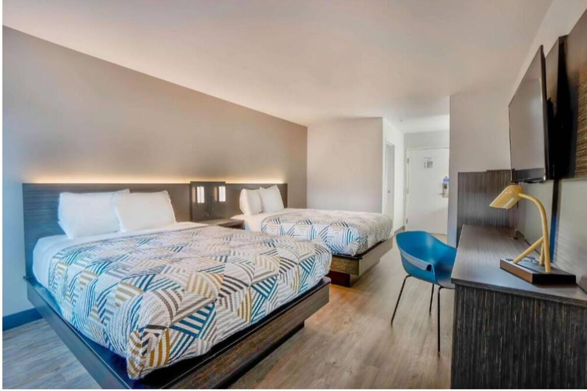 A modern hotel room with two beds, a desk, and a chair.