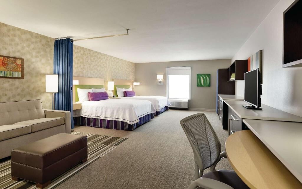 A hotel room with a bed, a desk, a chair, a sofa, and a television.