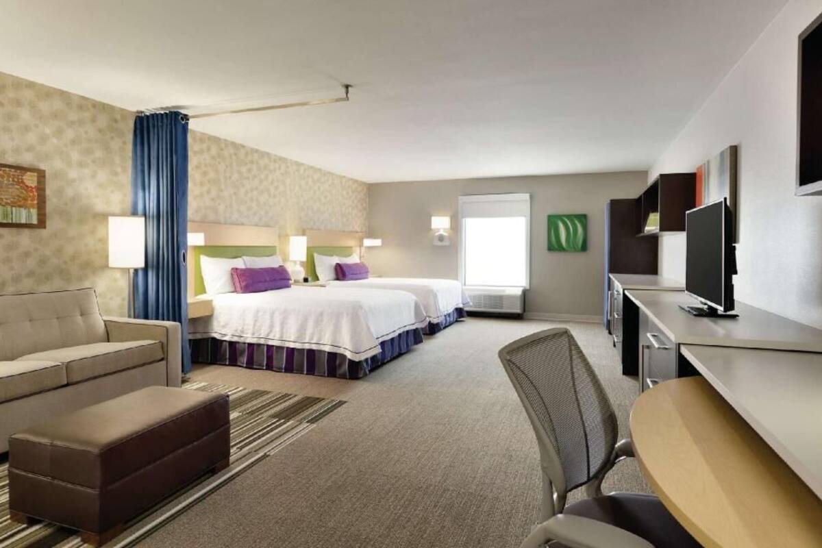 A hotel room with a bed, a desk, a chair, a sofa, and a television.