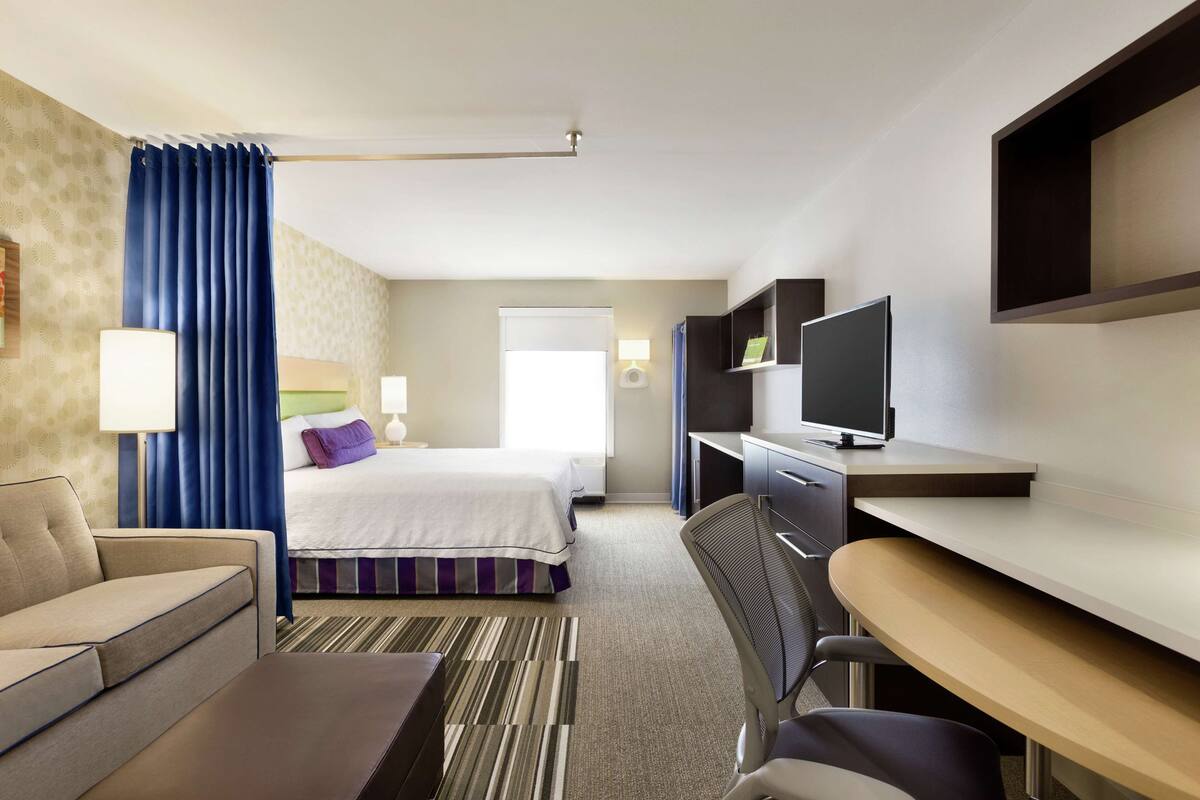 A hotel room with a bed, a desk, a chair, a TV, and a sofa.