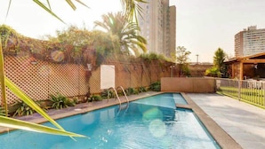 Uma piscina com deck de madeira, cercada por cerca e vegetação.