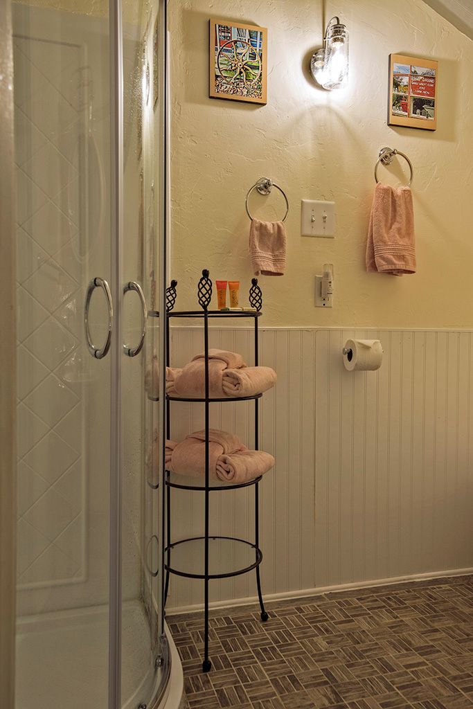 A bathroom with a glass shower door, a towel rack with pink towels, a toilet paper holder, and two framed pictures on the wall.