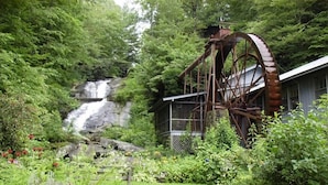Una estructura rústica de noria en un jardín exuberante, con una cascada al fondo.