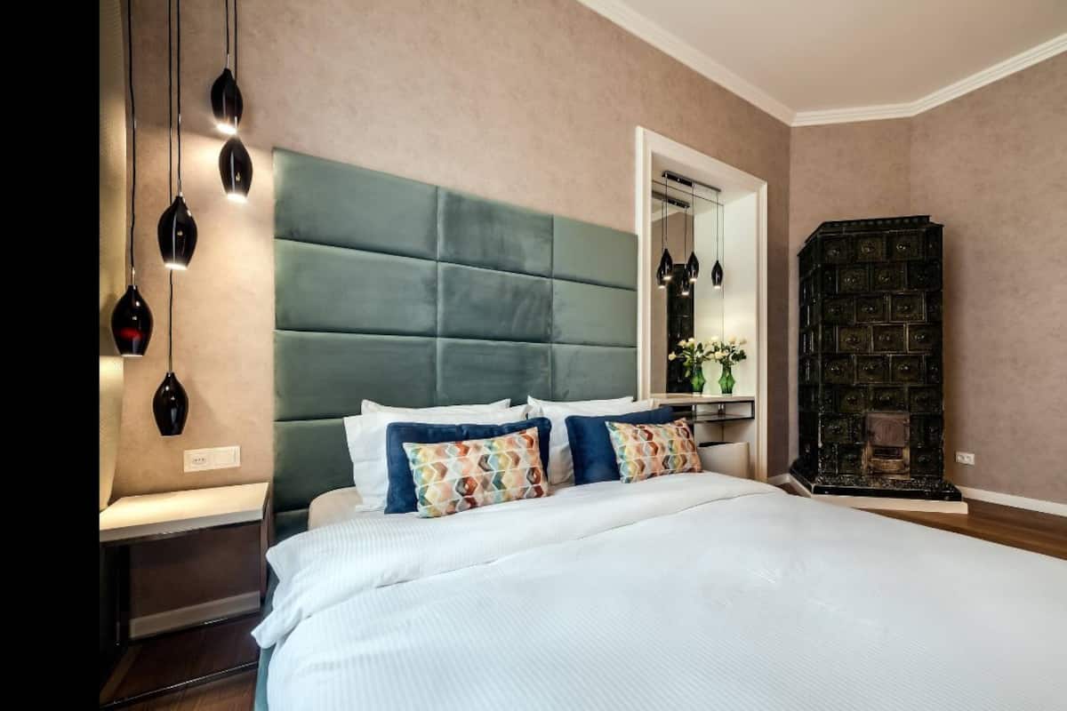 A bedroom with a large bed, a green upholstered headboard, a bedside table with a lamp, and a dark wooden cabinet.
