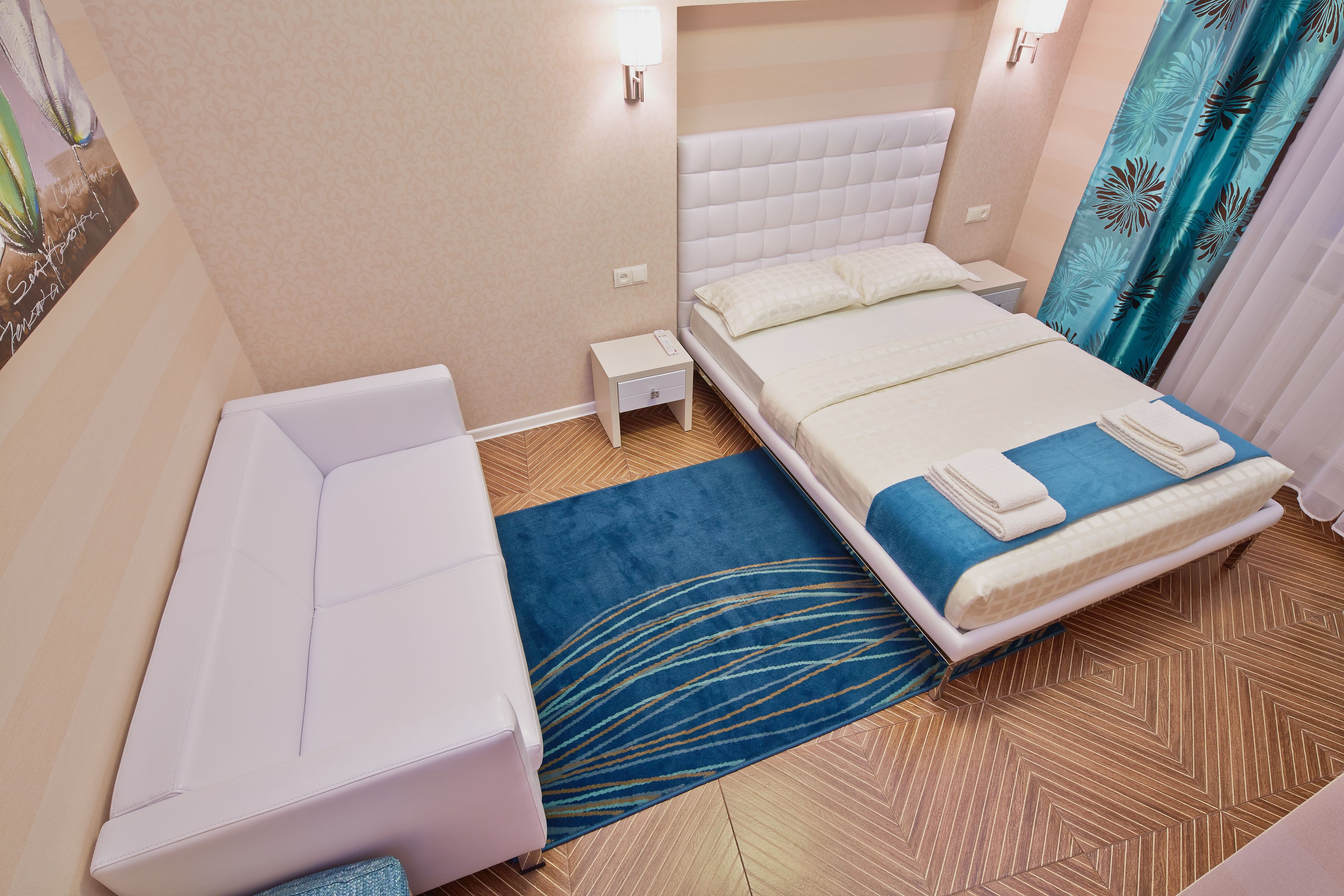 Una habitación de hotel con cama, sofá, mesita de noche pequeña y alfombra azul estampada.