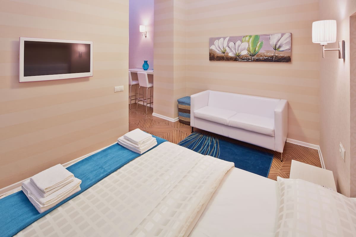 A hotel room with a bed, a white sofa, a TV mounted on the wall, and a painting above the sofa.