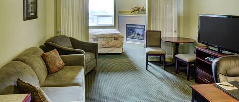 Habitación de hotel con sofá, sillón, televisor y chimenea.