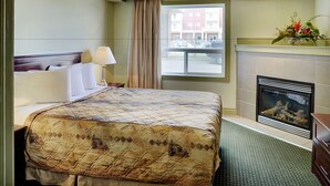 A hotel room with a large bed, a fireplace, a window with curtains, and a view of the street outside.