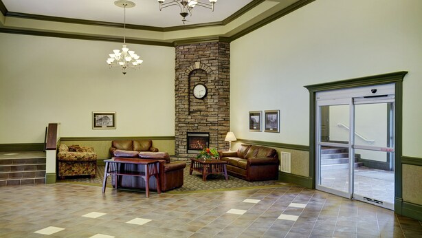 A lobby with a stone fireplace, leather sofas, a chandelier, and a staircase leading to an exit.