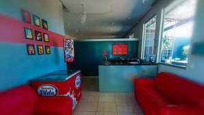 Una sala de estar moderna con sofás rojos, una zona de cocina con refrigerador, y un ventanal que proporciona luz natural.