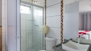 Un baño con ducha separada por vidrio, inodoro y lavamanos con espejo.