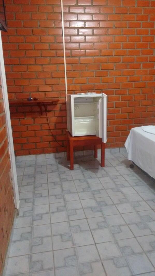 A room with a brick wall, a tiled floor, a small wooden table, and a white bed.