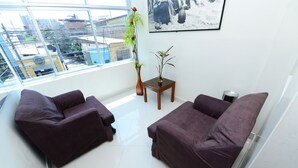 A modern living room with two dark sofas, a small wooden side table, and two potted plants.