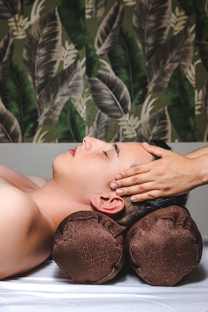 A person lying on a massage table with a pillow under their head, receiving a facial massage.
