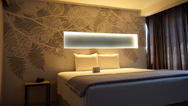 A hotel room with a bed, a bedside table, a wall-mounted TV, and a patterned wall.