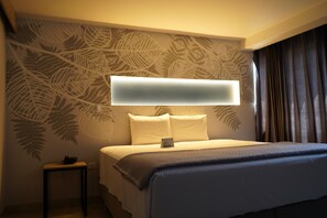 A hotel room with a bed, a bedside table, a wall-mounted TV, and a patterned wall.
