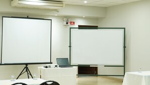 A conference room with two large projection screens, a laptop on a table, and several chairs.