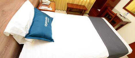 A neatly made bed with a white and gray bedspread, a blue pillow, and a wooden headboard.