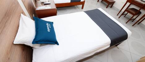 A hotel room with two beds, wooden headboards, a bedside table with a phone, a small wooden bench, and a desk with a chair.