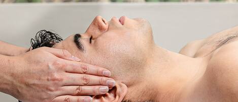 Una persona acostada en una bañera, con una toalla y una mano realizando un tratamiento facial.
