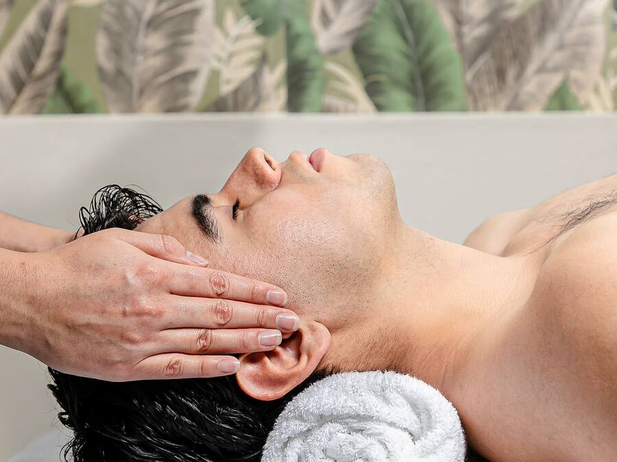 Una persona estesa en una banyera amb una tovallola i una mà fent un tractament facial.