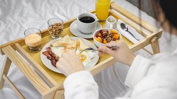 Un plateau de petit-déjeuner avec des toasts, des œufs, du bacon, un bol de fruits, un verre de jus d’orange et une tasse de café.