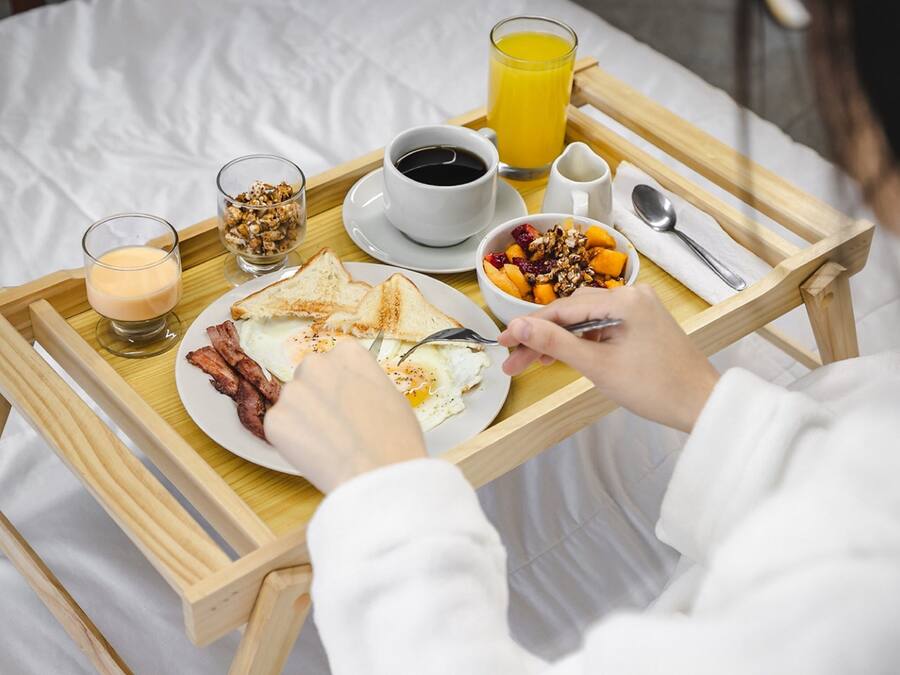 Un plateau de petit-déjeuner avec des toasts, des œufs, du bacon, un bol de fruits, un verre de jus d’orange et une tasse de café.