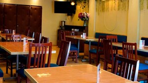 A dining area with multiple tables and chairs, ceiling fans, and a wall-mounted television.
