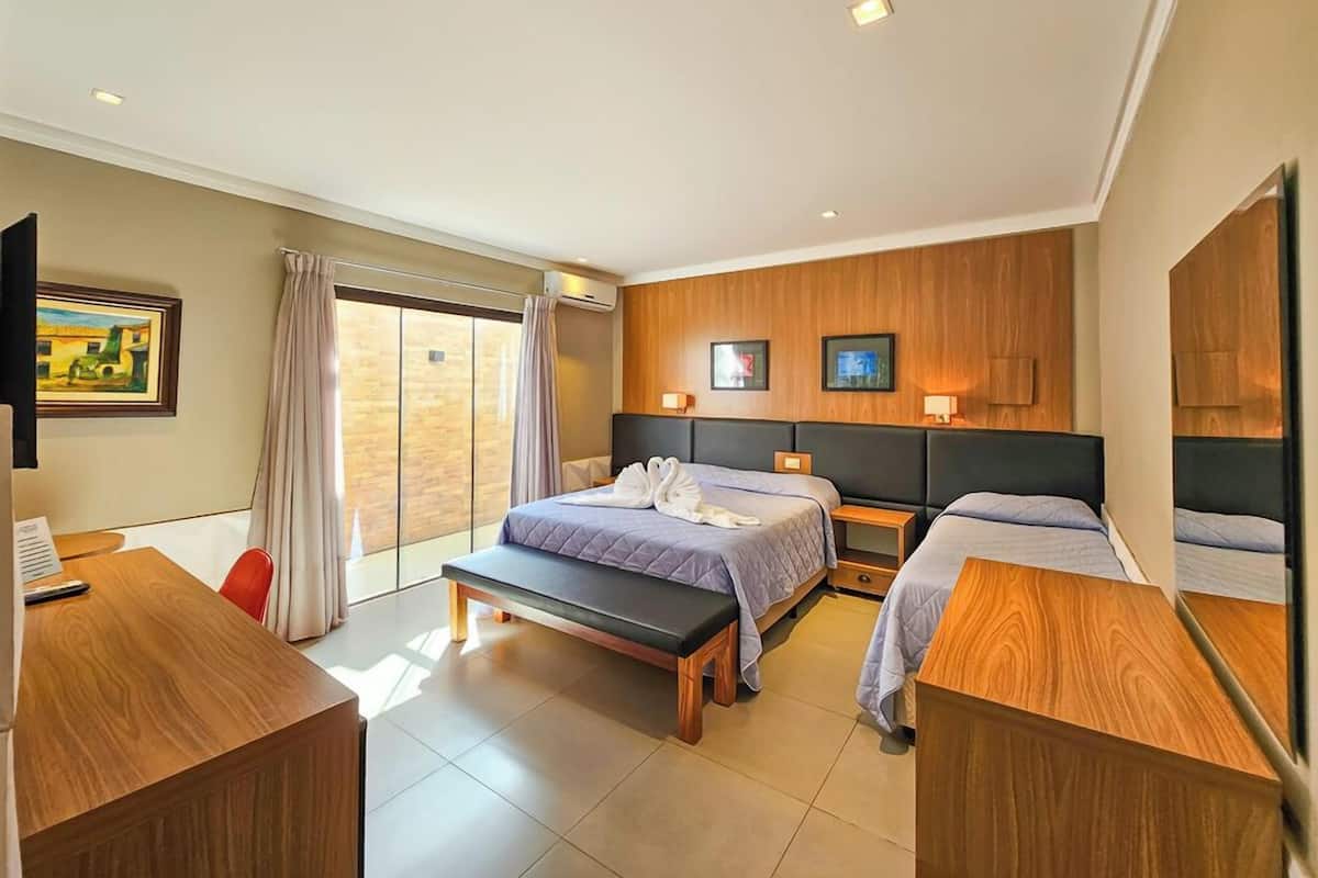 A hotel room with two beds, a desk, and a large window.