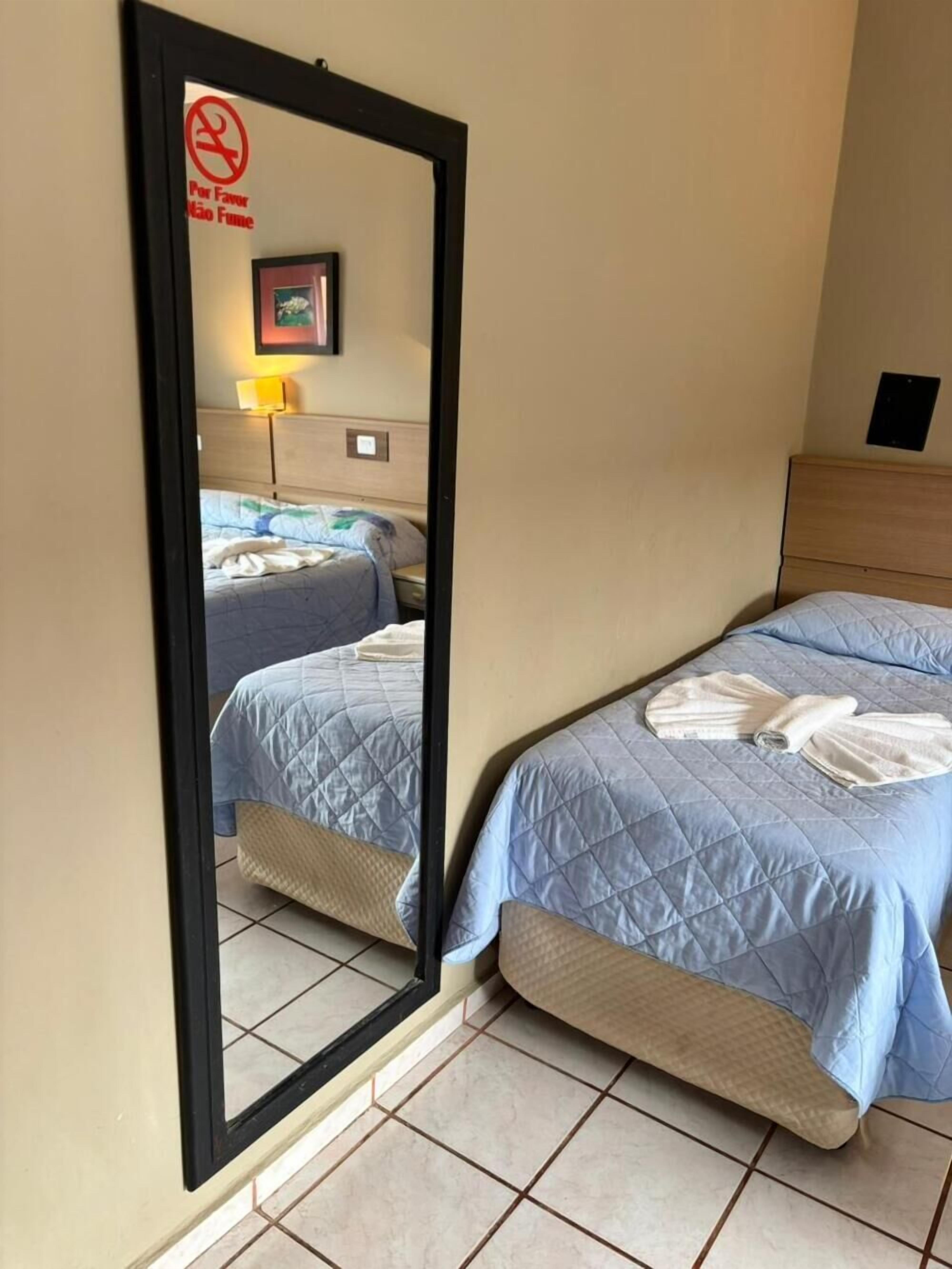 Ein Hotelzimmer mit zwei Betten, einem Spiegel, einer Wandleuchte und einem gerahmten Bild.