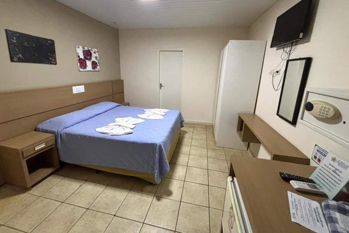 A hotel room with a bed, a desk, a TV, a mirror, and a door.