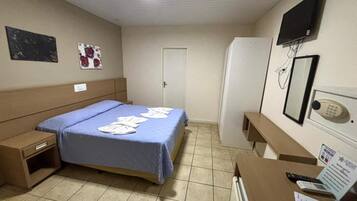 Una habitación de hotel con una cama, un escritorio, un televisor, un espejo y una puerta.