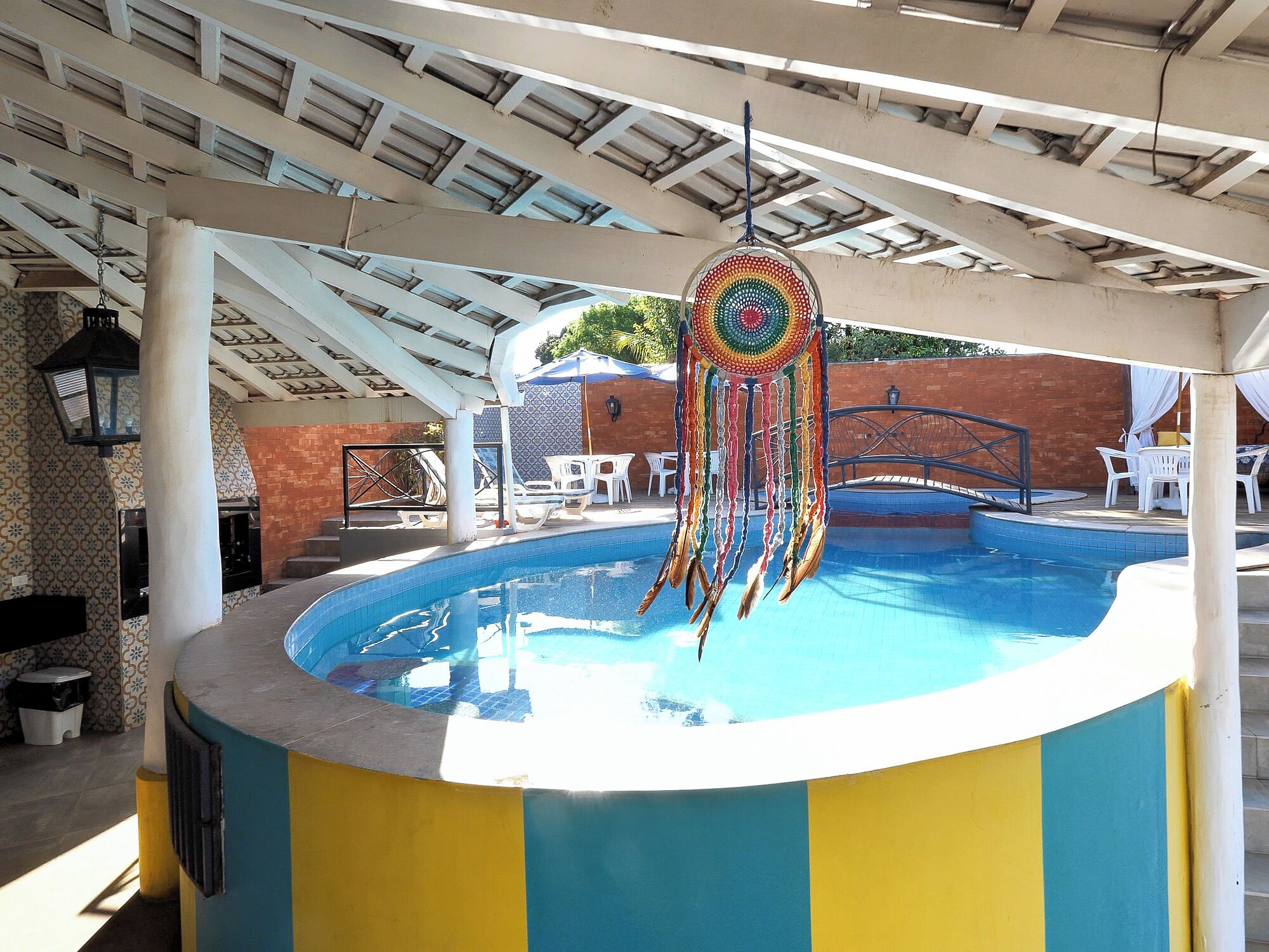 Un área de piscina con una decoración llamativa de atrapasueños, sillas blancas y un porche cubierto.