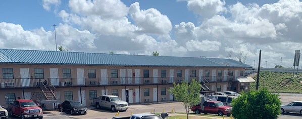 A motel with a long, single-story building, multiple rooms, and a parking lot with several vehicles. - Loma Alta Motel (Laredo)