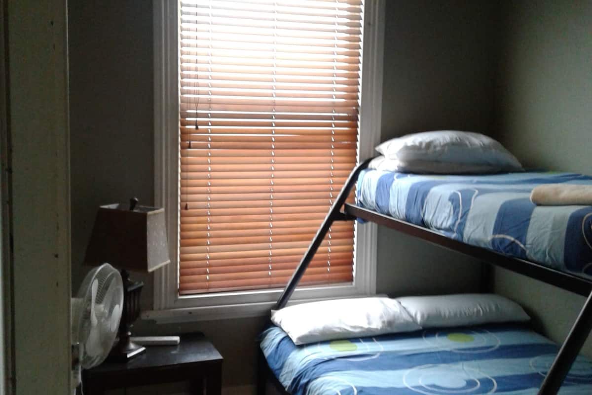 Una habitación pequeña y tenuemente iluminada con una litera, un escritorio con lámpara y una ventana con persianas.