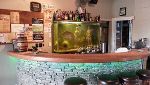 A bar area with a stone counter, multiple stools, and a large fish tank. - Shooters Saloon Bar Hotel & Cabins (Auckland)