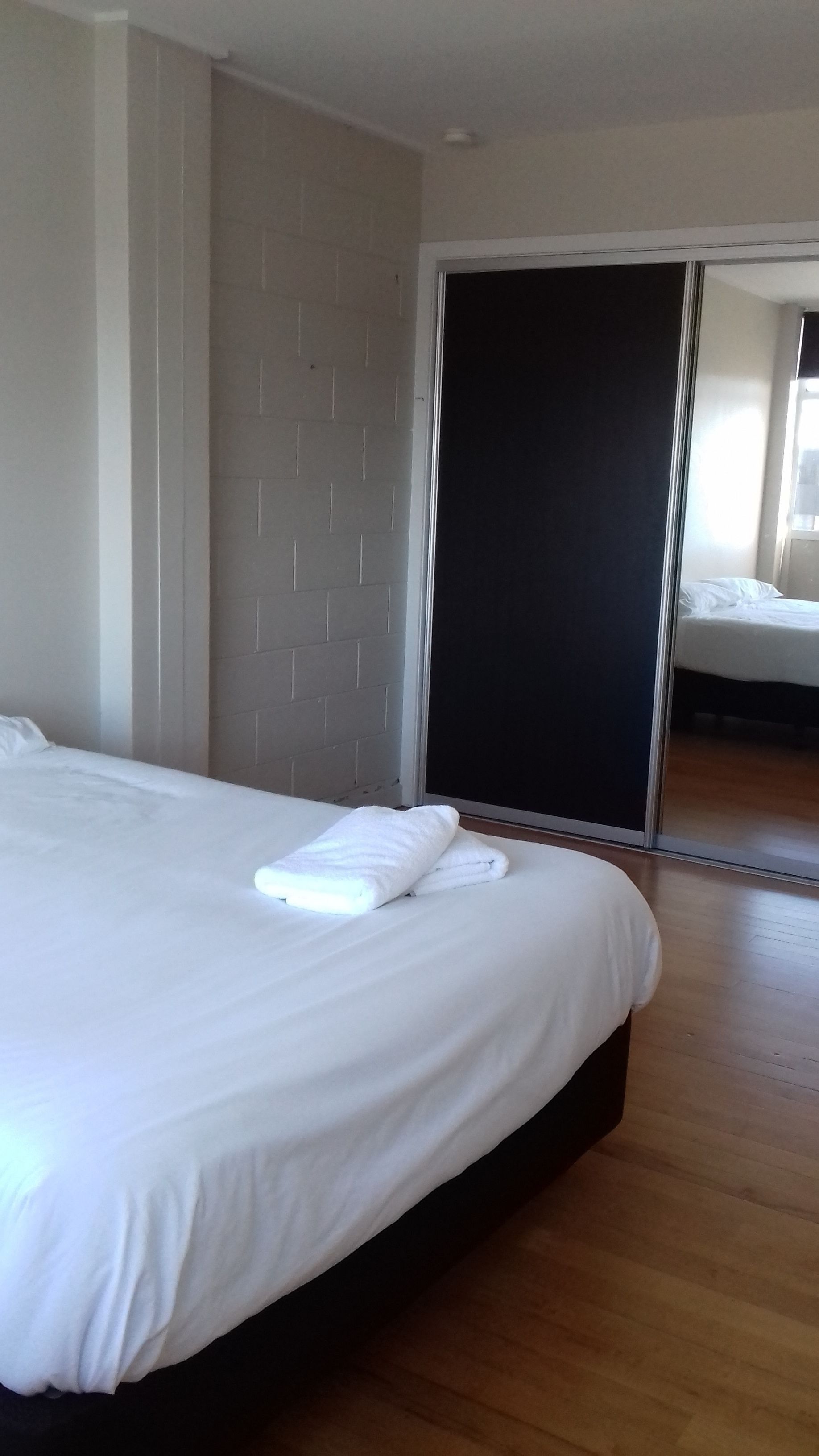 A modern hotel room with a large bed, a sliding door closet, and a wooden floor.