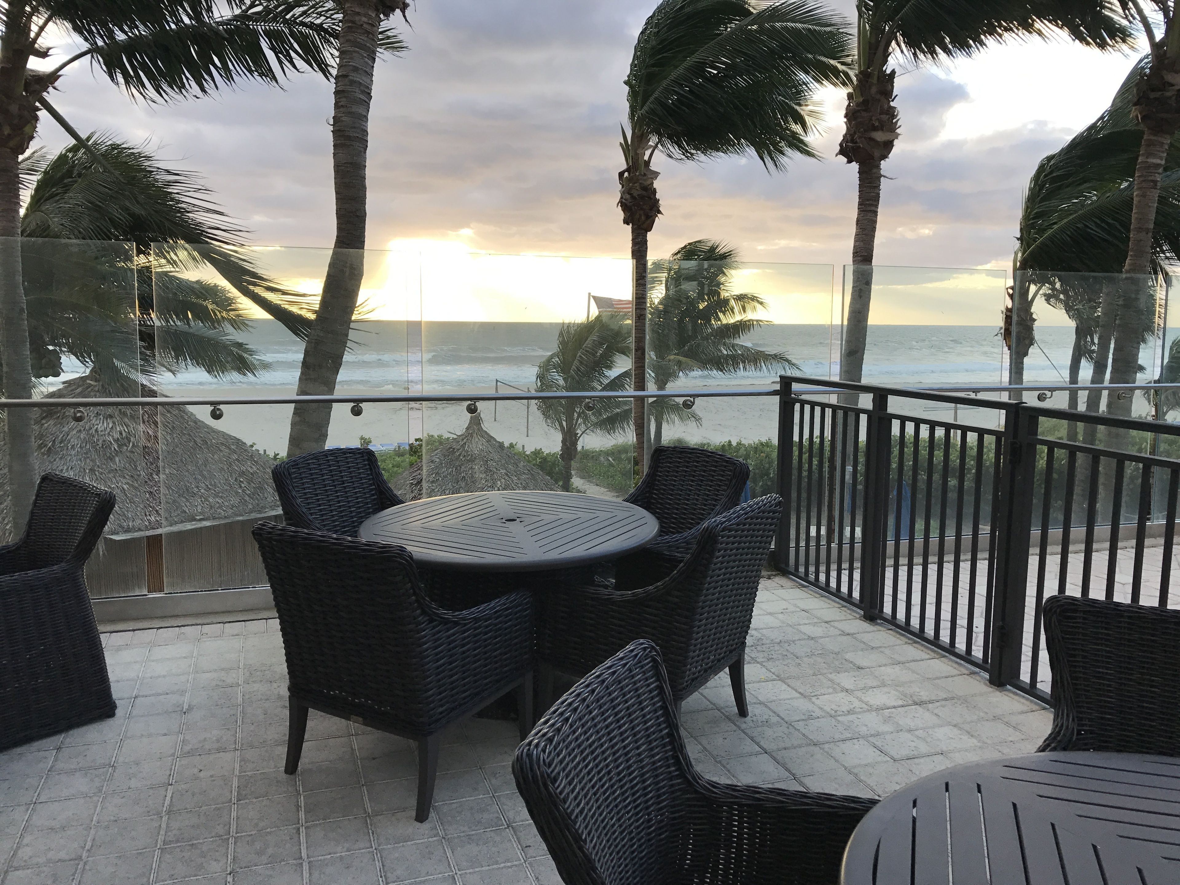 A balcony with wicker furniture and a view of the ocean at sunset.