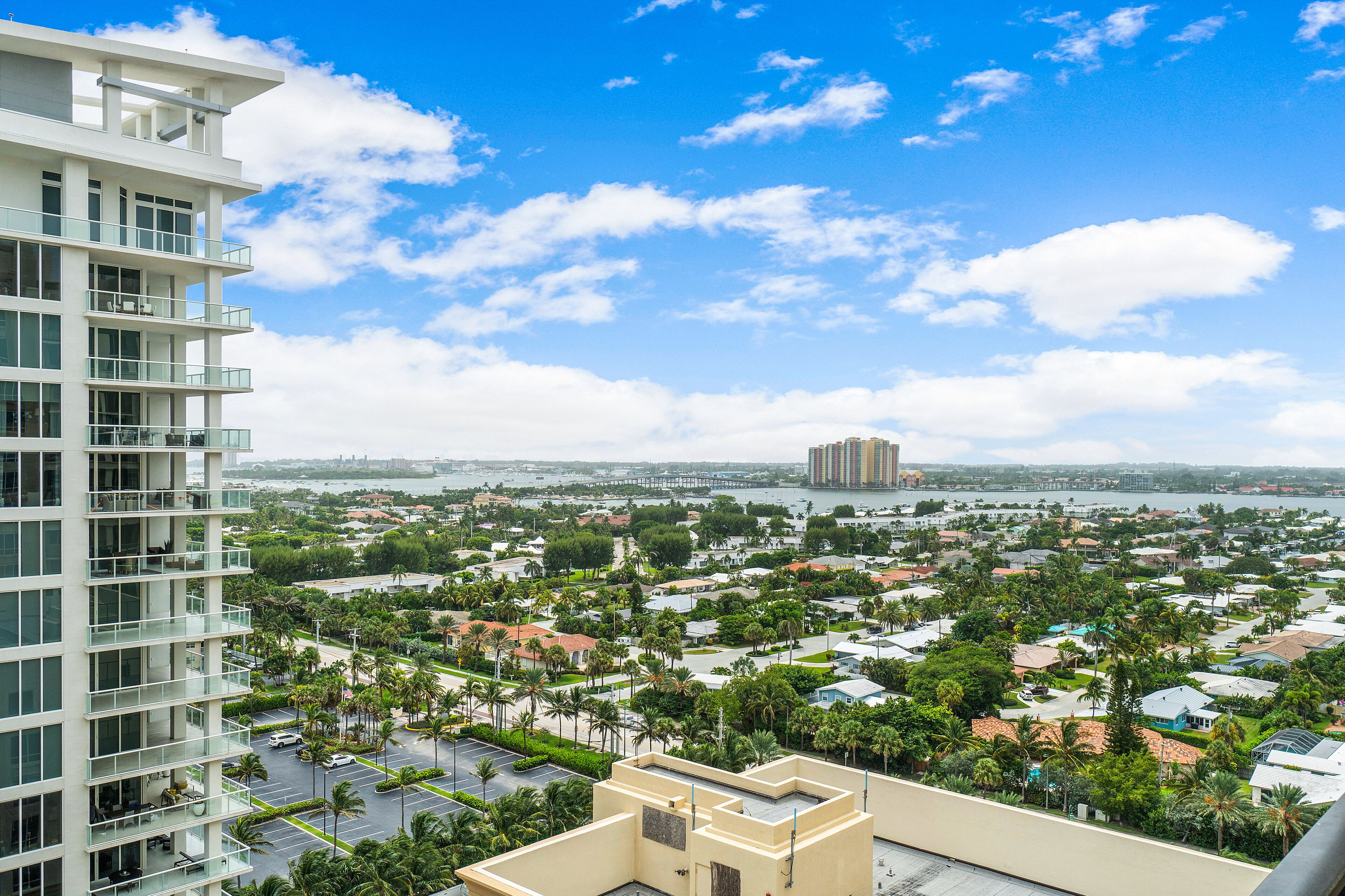 A high-rise hotel with multiple balconies, a view of a coastal cityscape, and a marina in the distance.