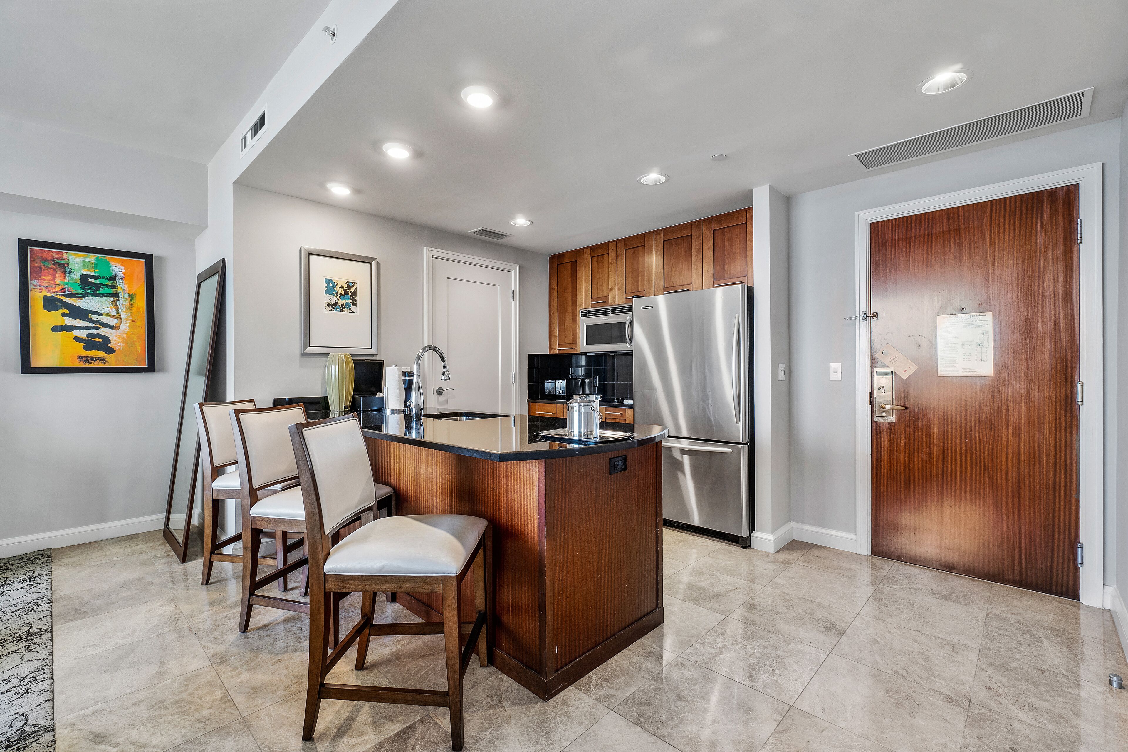 A modern kitchen with a central island, wooden cabinets, stainless steel appliances, and a dining area with chairs.