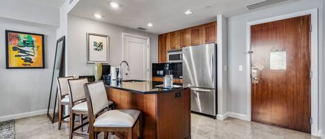 A modern kitchen with a central island, wooden cabinets, stainless steel appliances, and a dining area with chairs.